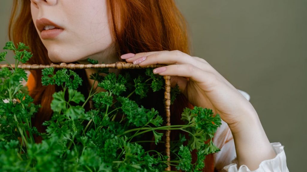 Aesthetic portrait of a woman with red hair holding fresh parsley.