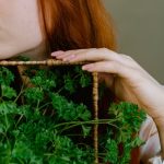 Aesthetic portrait of a woman with red hair holding fresh parsley.