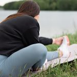 Woman doing stretching exercises on a yoga mat outdoors by a serene lake.