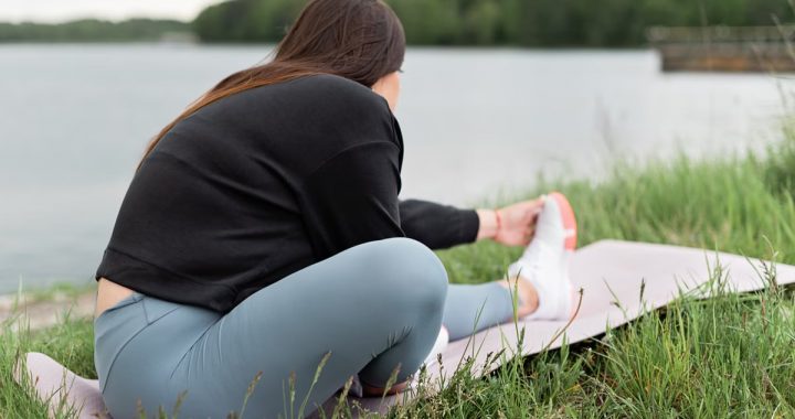 Woman doing stretching exercises on a yoga mat outdoors by a serene lake.